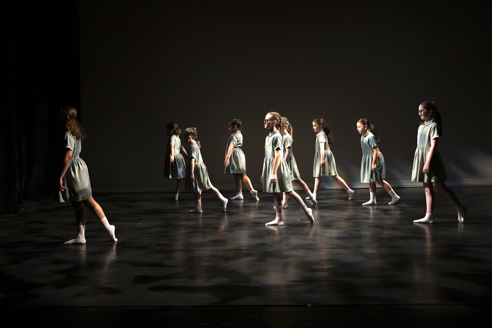 Junior dancers walking in formation on a dark stage